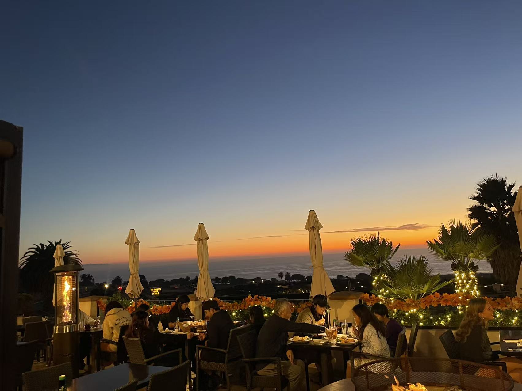 Guests dining on the ocean-view patio at sunset